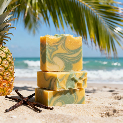 Stack of yellow and green marbled soap bars on a sandy beach with a pineapple and vanilla beans.