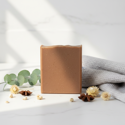 Still Water artisan soap bar with smooth rich chocolate brown finish standing upright on a sunlit white stone bathroom counter with linen towel and botanical accents