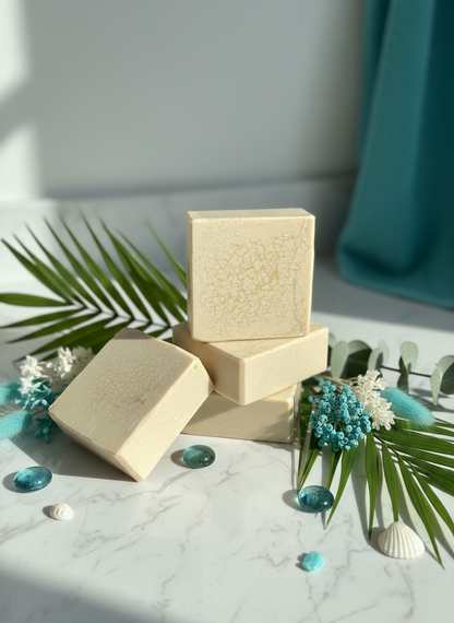 Beige soap bars with a textured surface on a marble surface with greenery and blue stones.