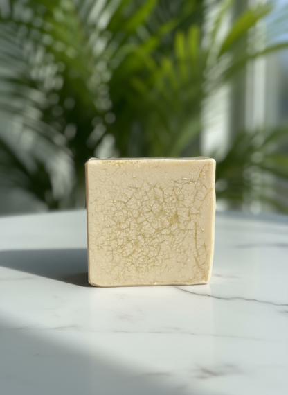 Square beige bar of soap with a cracked texture on a marble surface with a blurred green plant background
